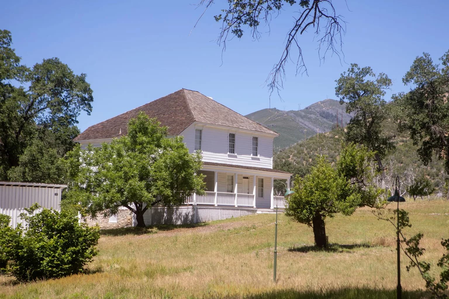 White farmhouse on a rural California property with oak trees and dry grass