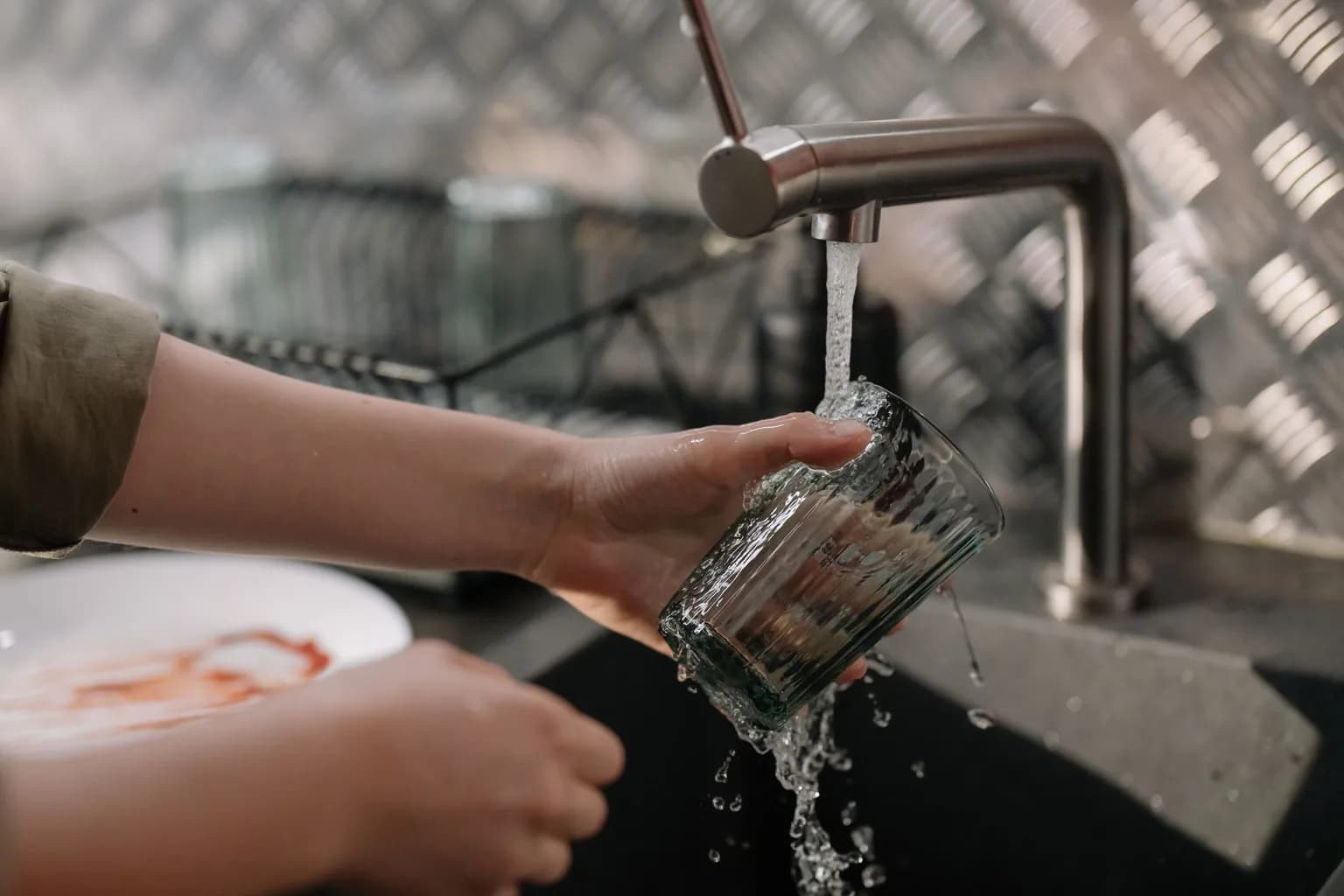 Glass being rinsed under a running kitchen tap